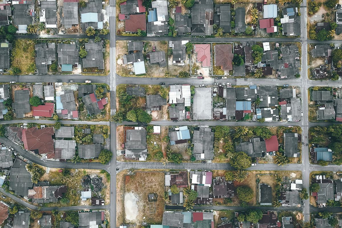 Overhead view of roadways and roofs of aged dwelling housing complexes near trees in suburb