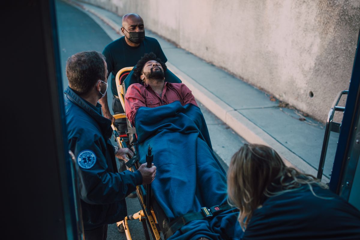 Paramedics assist a patient on a stretcher during an emergency response. Outdoors setting.
