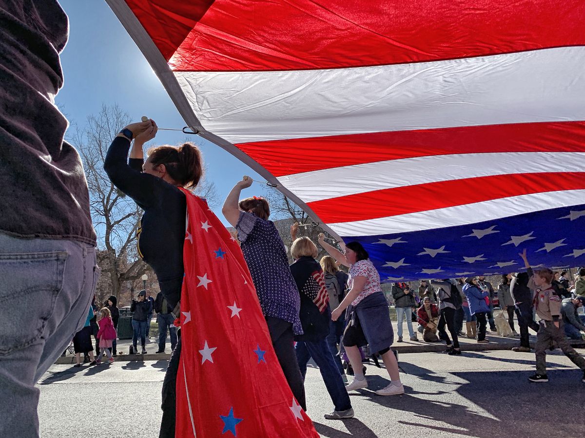 People celebrating under a massive American flag at a parade in Denver, CO, showcasing patriotism and community spirit.