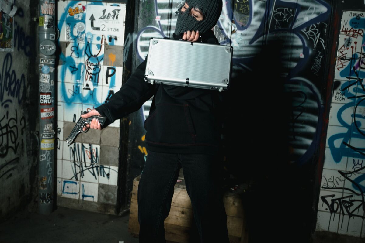 person-in-black-jacket-with-mask-holding-a-silver-briefcase-and-gun