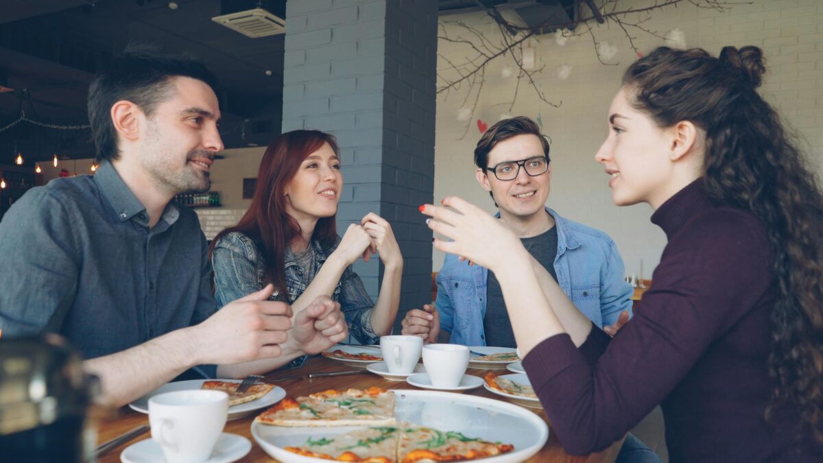 Friends having a delightful conversation over pizza and coffee in a cozy cafe.