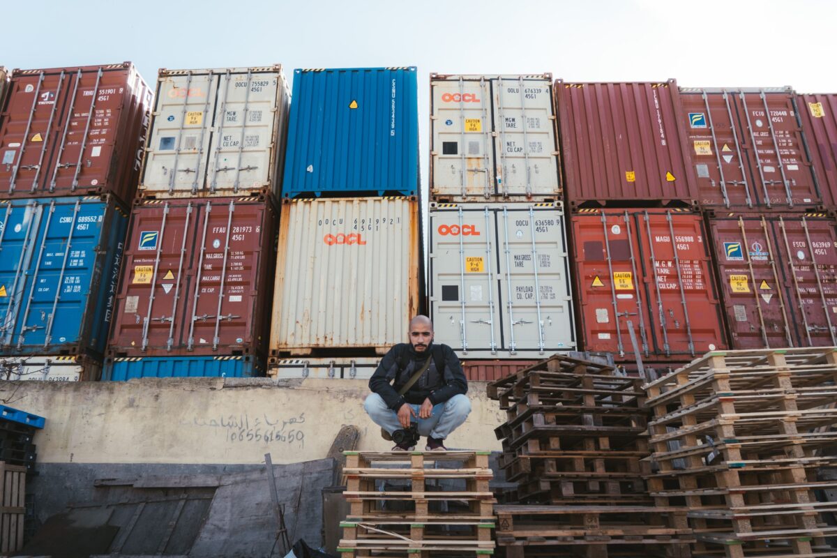 Trump Unveils New Tariffs on 60 U.S. Trading Partners as Global Trade Tensions Escalate. 3 man-crouching-near-stacked-shipping-containers