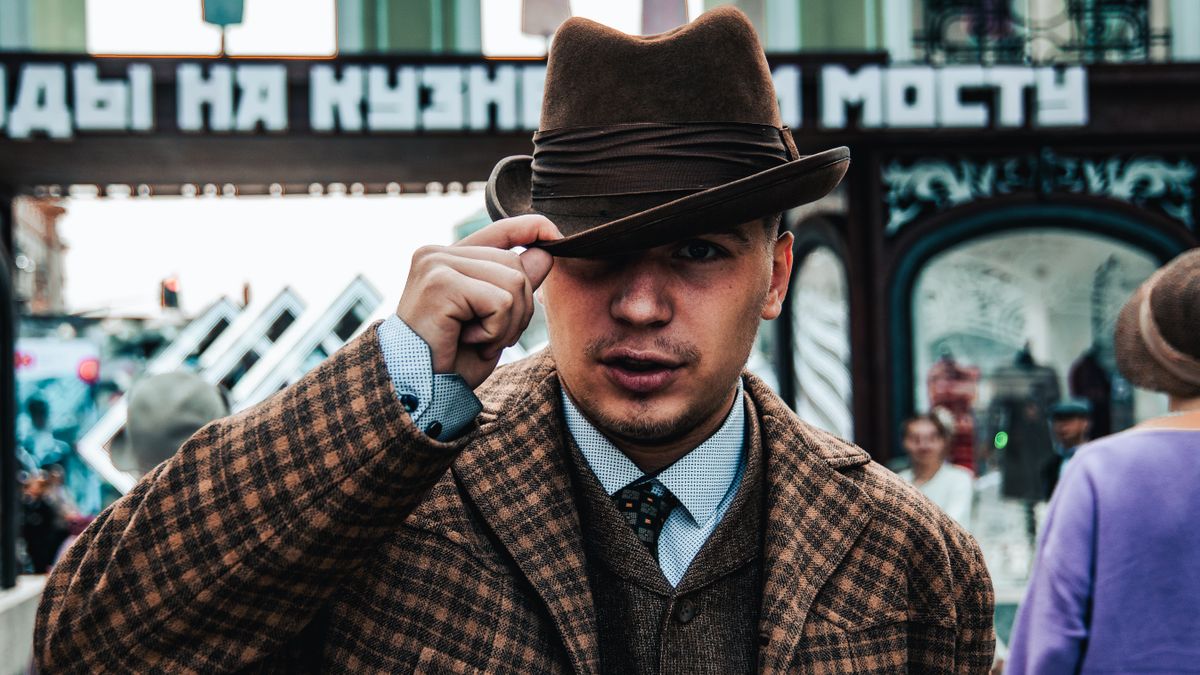 8 Men’s Fashion Choices That Scream “Notice Me Now.” 4 Portrait of a stylish man in a brown plaid coat and fedora, captured with selective focus on a city street.