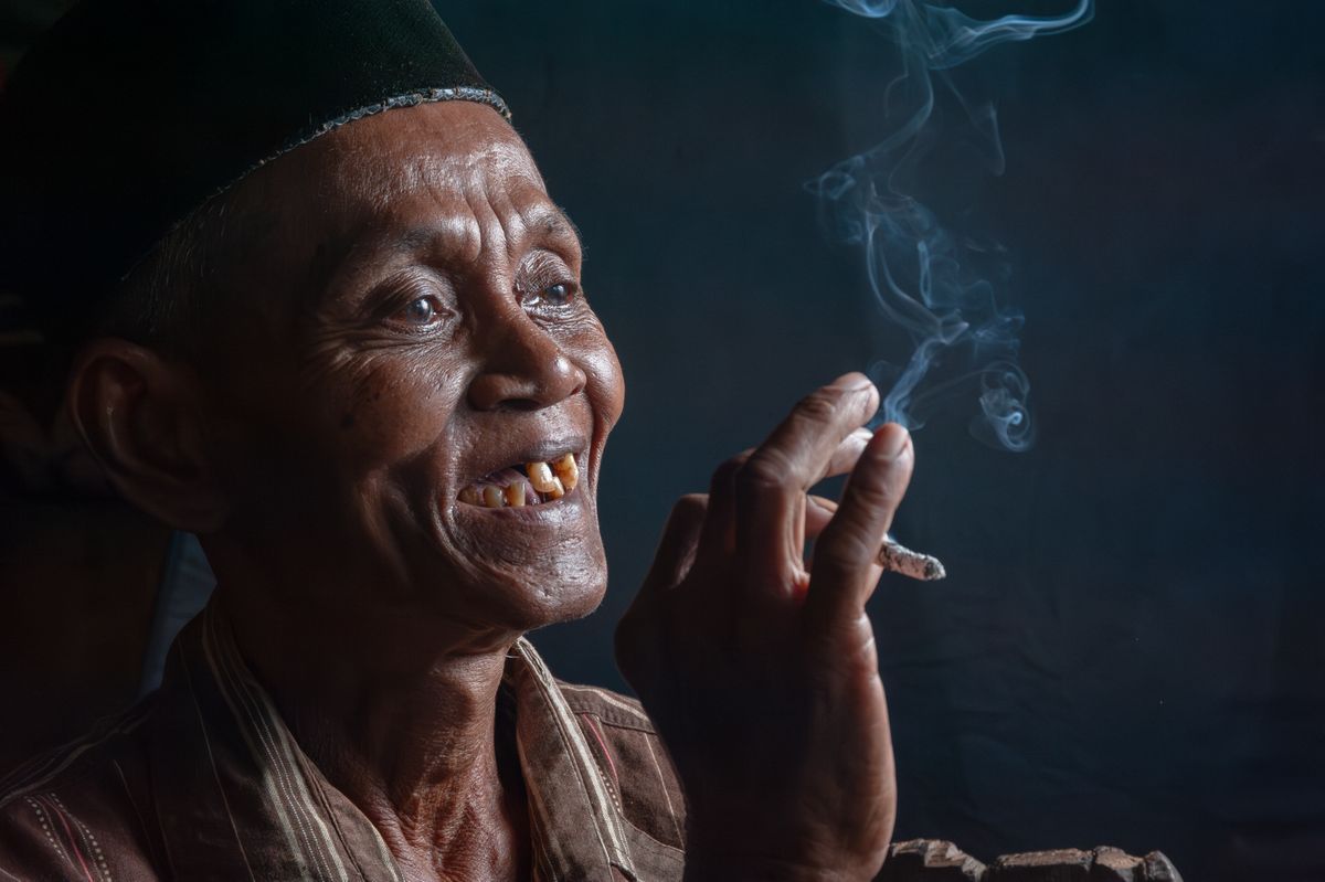Portrait of an elderly man smoking a cigarette with a joyful expression indoors.