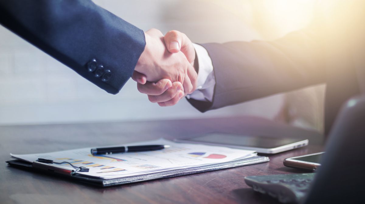 Zohran Mamdani Says ICE Should Be Abolished Despite Working Relationship With Trump 3 Professional handshake agreement over business charts in an office setting.