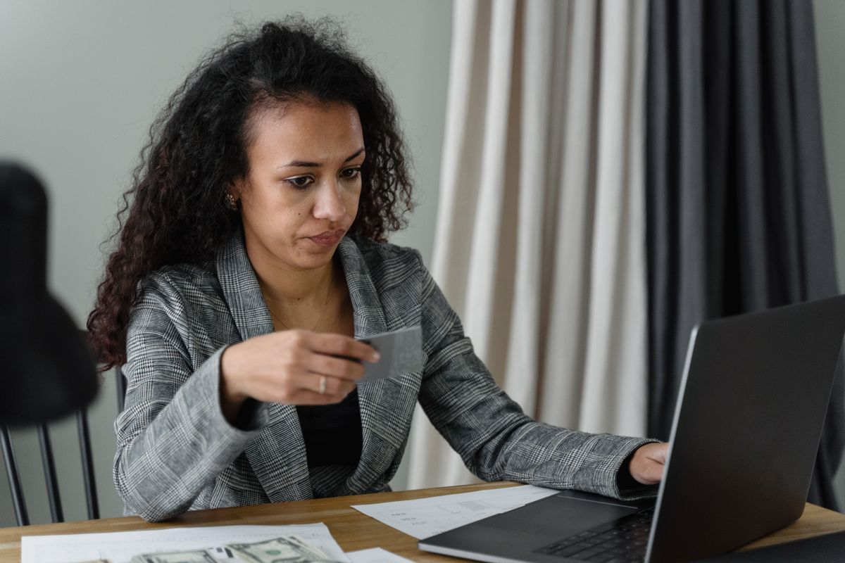 What Happens If You Do Not Pay a Deceased Person’s Credit Card Debt 2 Professional woman at desk with credit card, laptop, and cash. Expression of concentration.