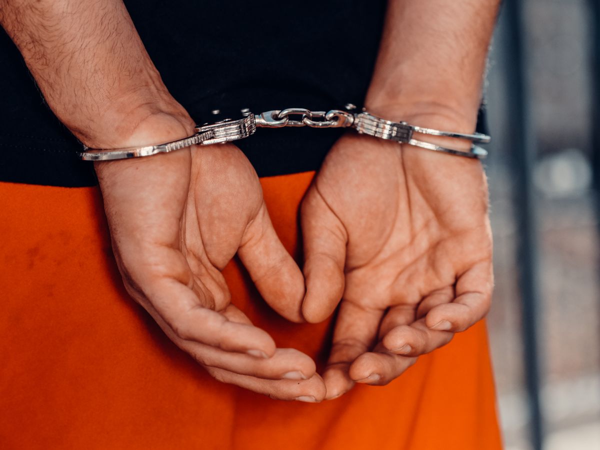 Rear view of handcuffed person in orange uniform, highlighting law enforcement and justice themes.