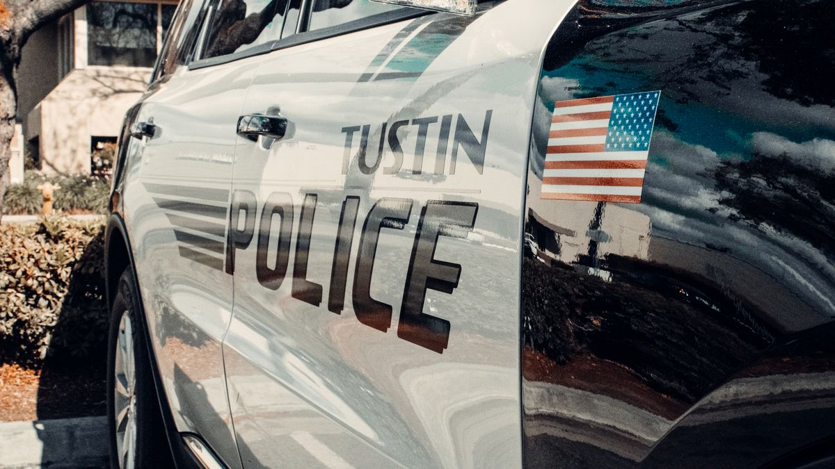 Reflective image of a Tustin police car parked outdoors with an American flag emblem.