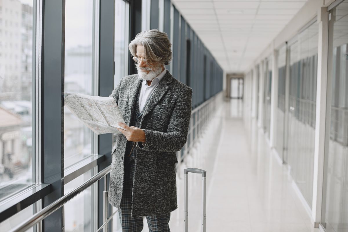 12 Everyday Habits That Will Fade With the Baby Boomer Generation 1 Senior man with beard reads map by glass windows in modern hallway with luggage. Printing Directions Before a Trip