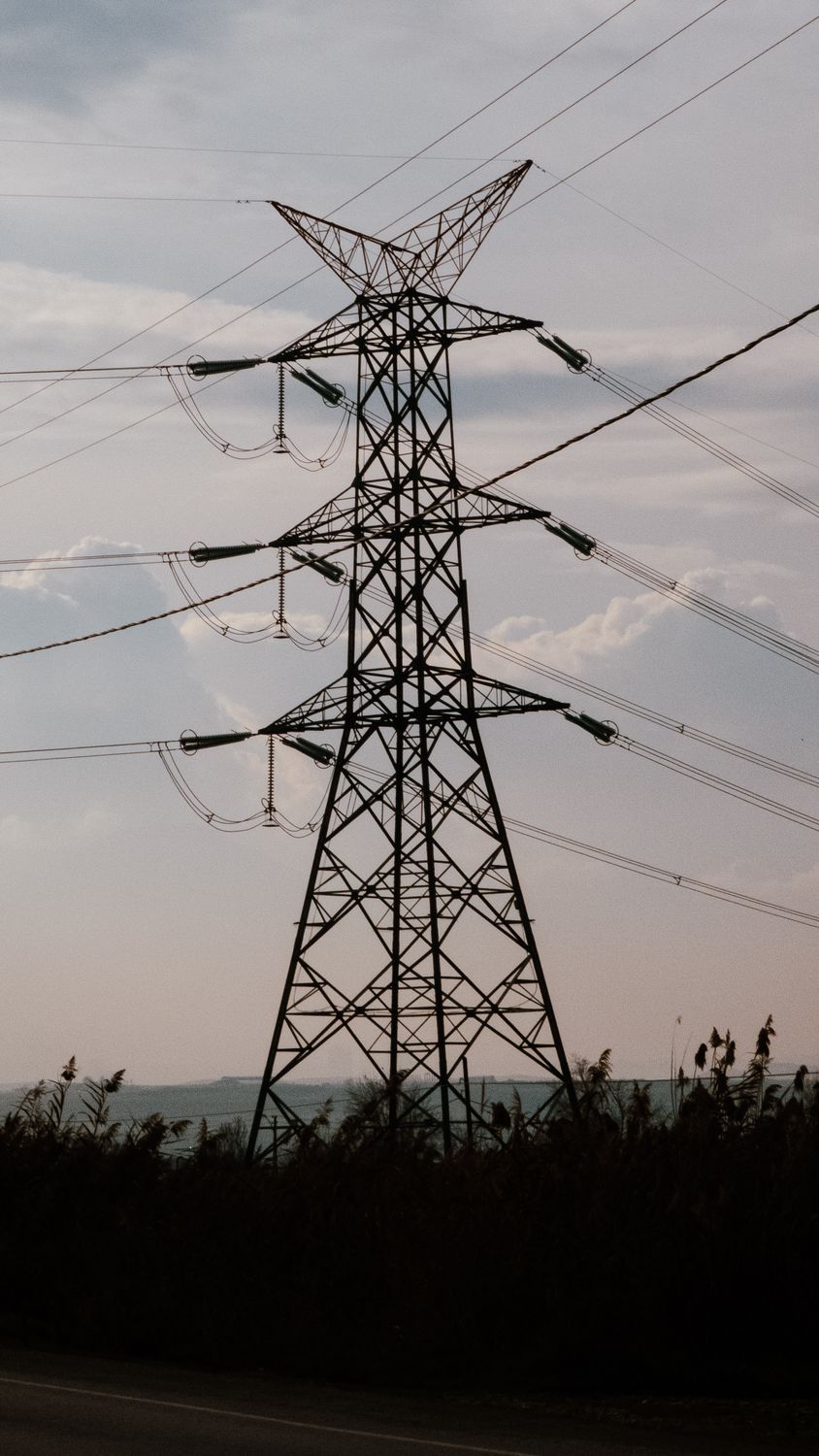 Silhouette of a high voltage power transmission tower against a cloudy sky.