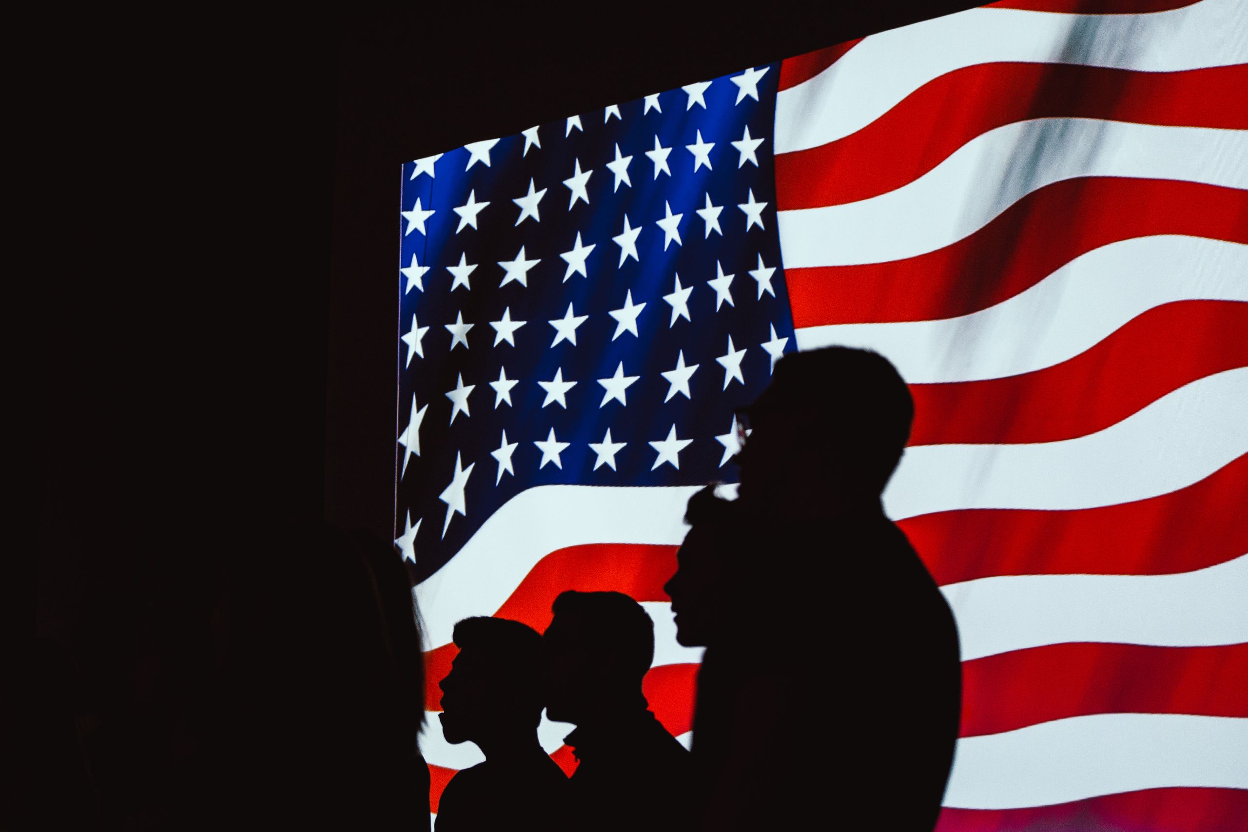 Obama Center’s Bold Chicago Tower Opens a Bigger Fight Over Taste, Legacy, and Who Gets to Define a President 2 Silhouetted figures in front of a bright, wavy American flag create a patriotic scene.