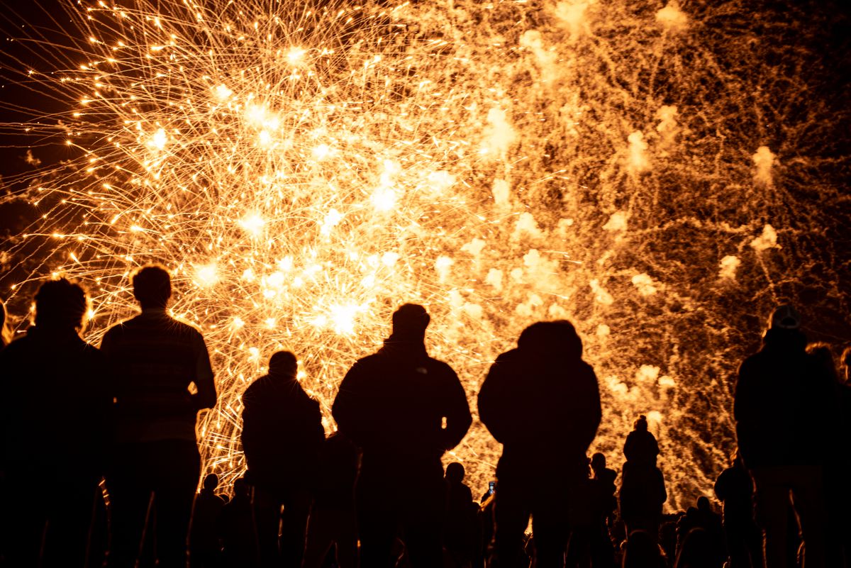 Silhouettes watching vivid golden fireworks explode in a dynamic night sky celebration.
