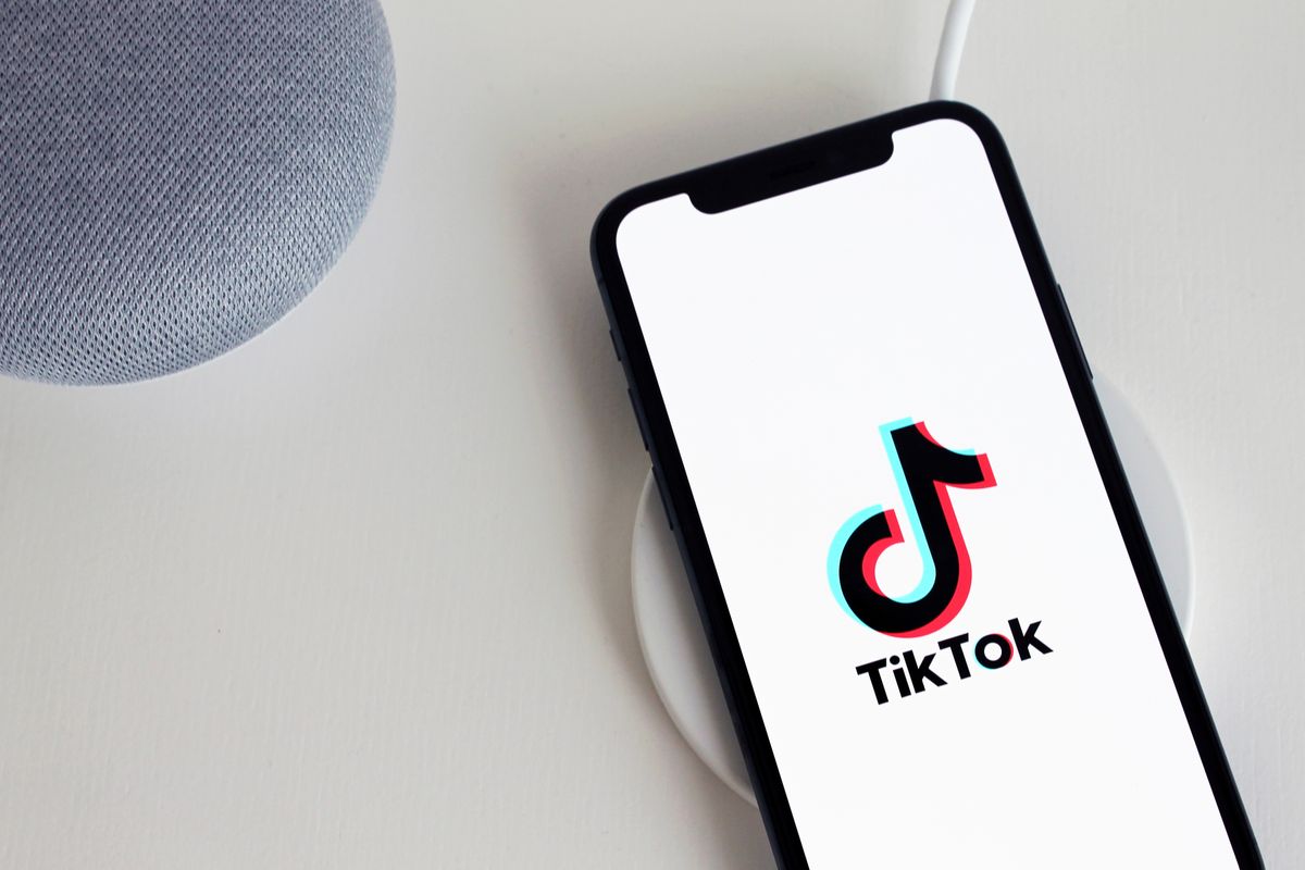 Can You Bring Iced Coffee to a Job Interview? TikTok Debate Sparks Conversation 1 Smartphone displaying TikTok app logo, placed on a wireless charger beside a smart speaker.