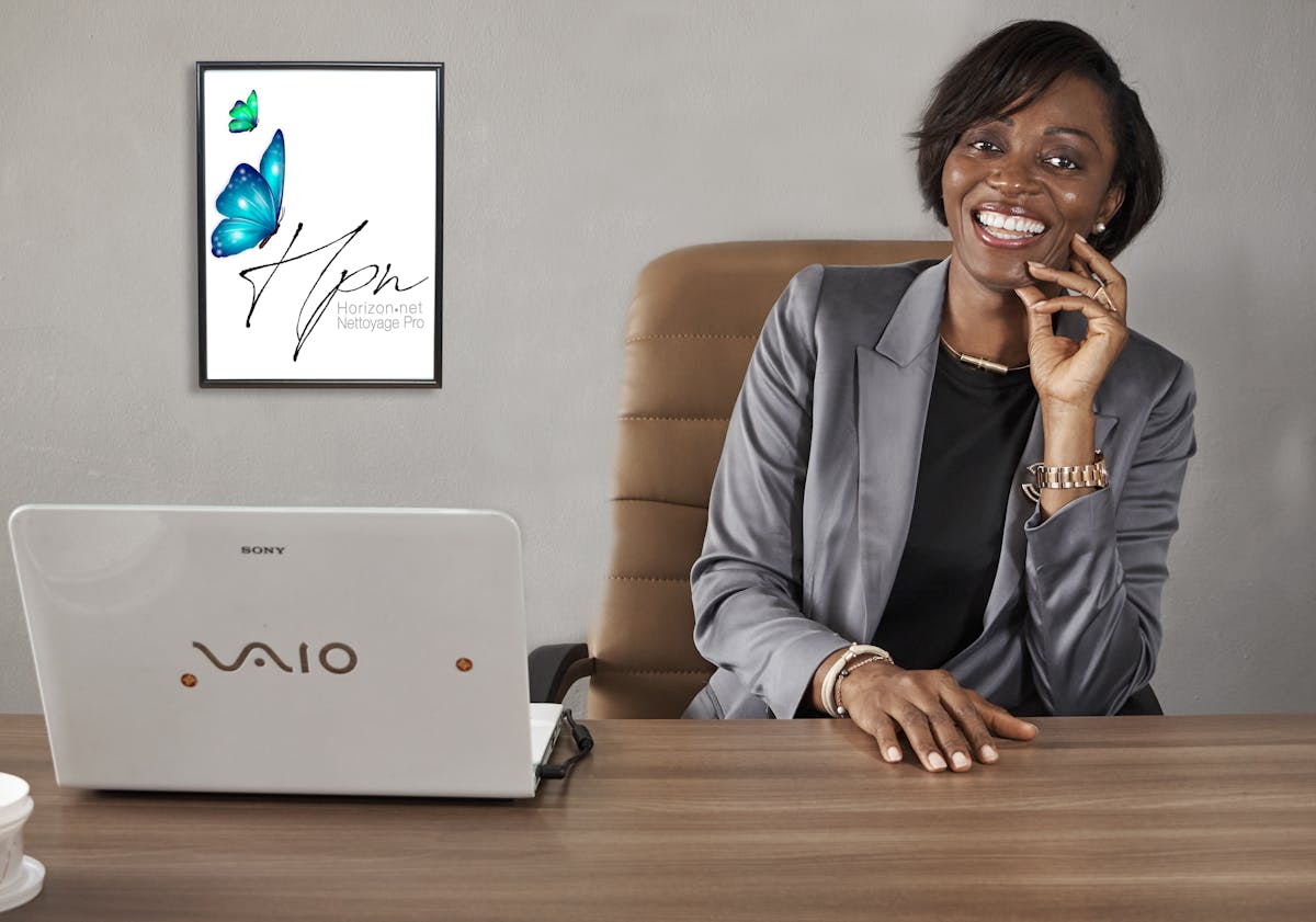 Smiling African American businesswoman in a gray blazer sitting at a desk in an office setting.