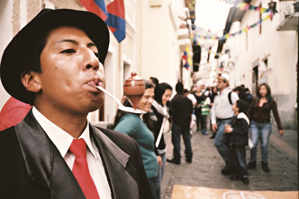 Street performer balancing on spoon, surrounded by festive Quito crowd.