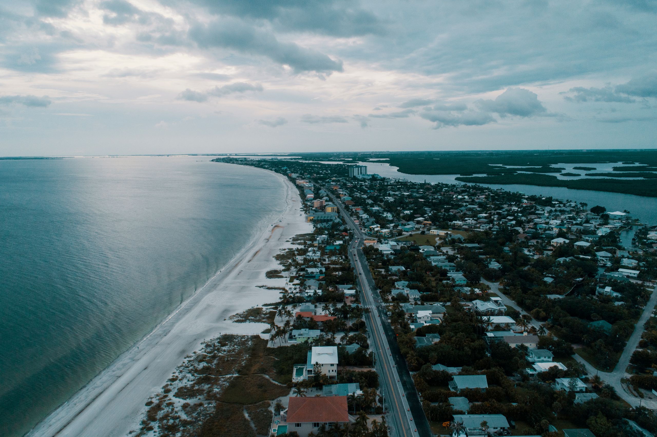 Stunning aerial view of a coastal city lined with houses and a vast, calm ocean under a cloudy sky.