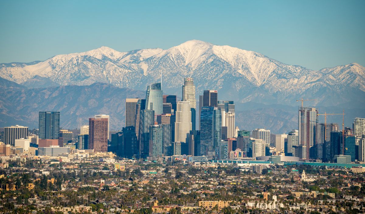 Stunning aerial view of downtown Los Angeles with snowy mountains in the background, highlighting the city skyline.