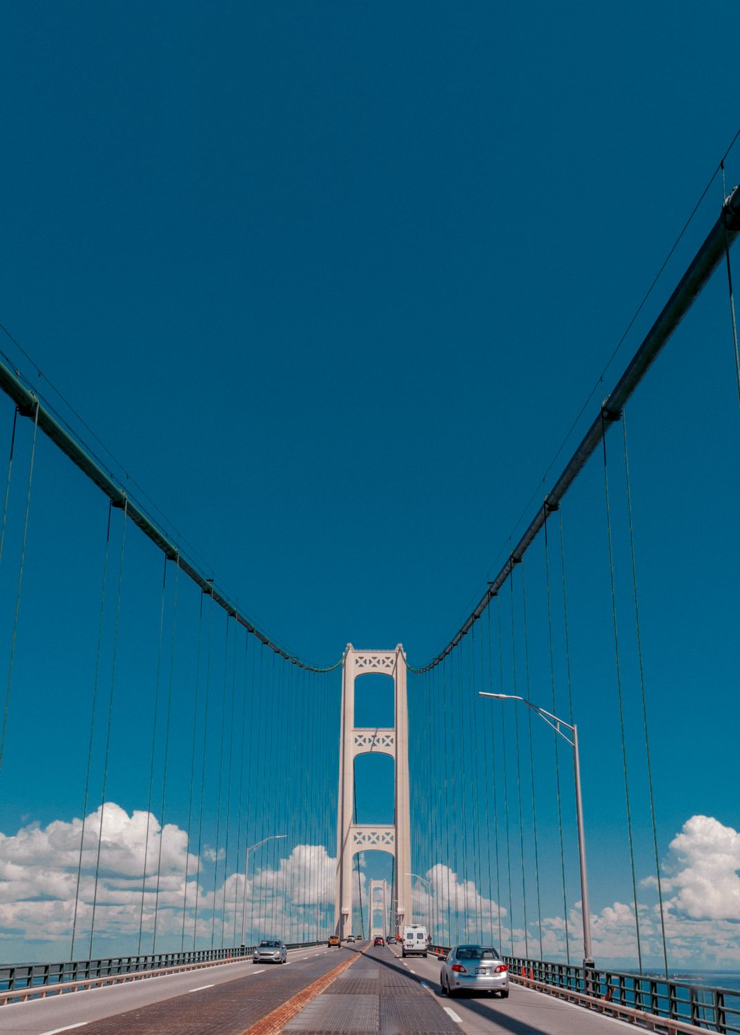 Bridges in the USA Aren’t as Safe or Simple as They Seem 2 Stunning view of a suspension bridge with cars under a vibrant blue sky, showcasing symmetry and urban architecture.