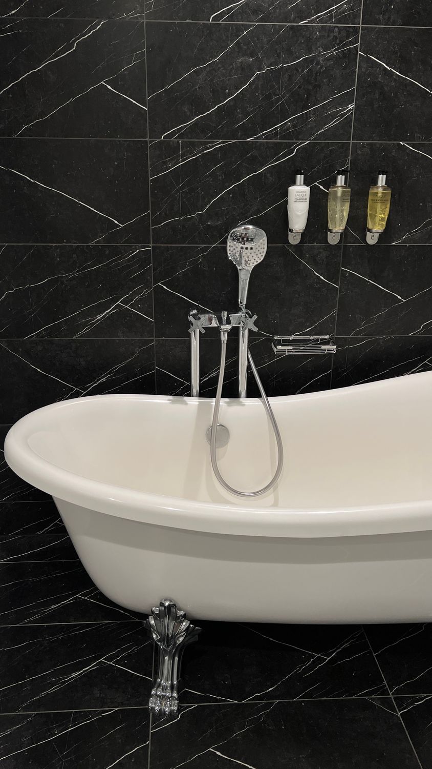 Stylish white bathtub against black marble wall in a contemporary bathroom setting.