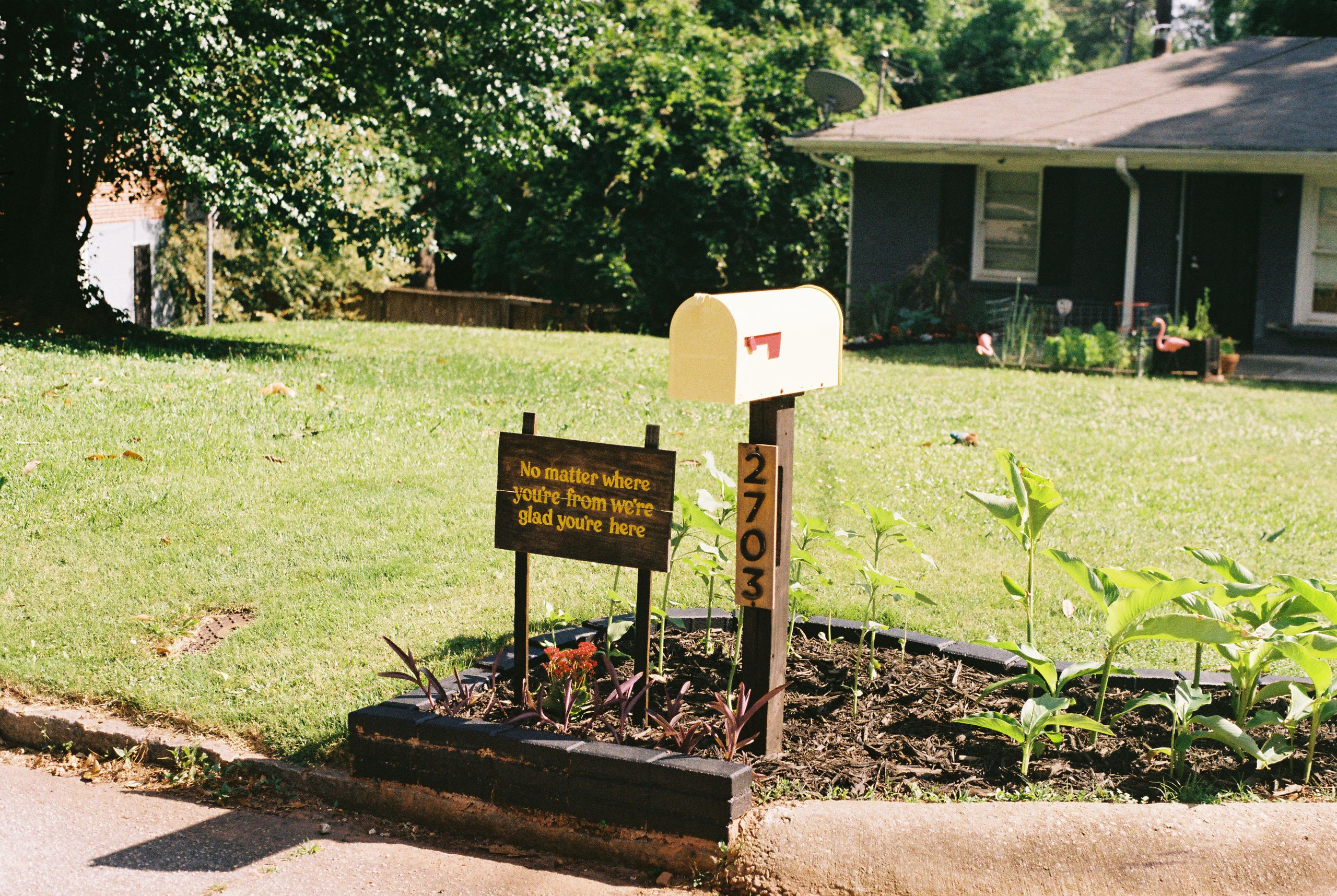 Older Americans Paid Into the System. Now Their Benefits Feel Hidden in Fine Print 2 Suburban house with plants and welcoming sign by mailbox on a sunny day.