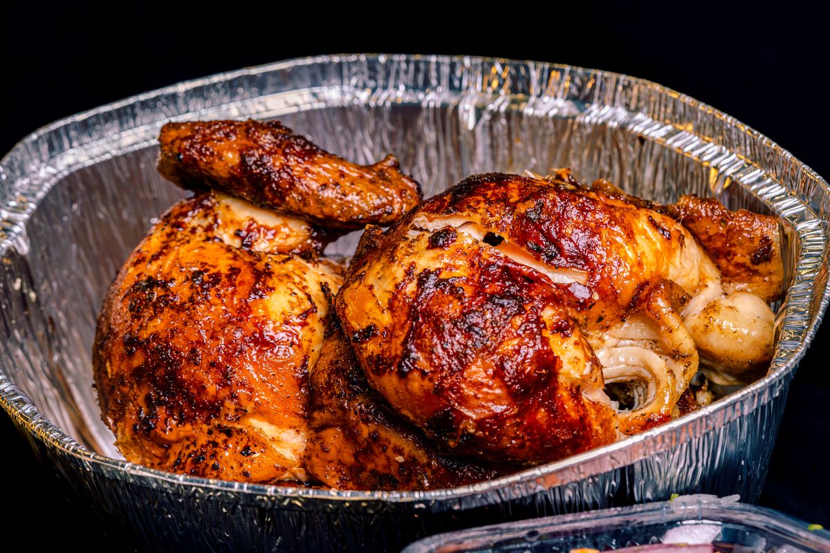 Succulent roasted chicken with crispy skin in a foil tray, perfect for dining or takeaway.