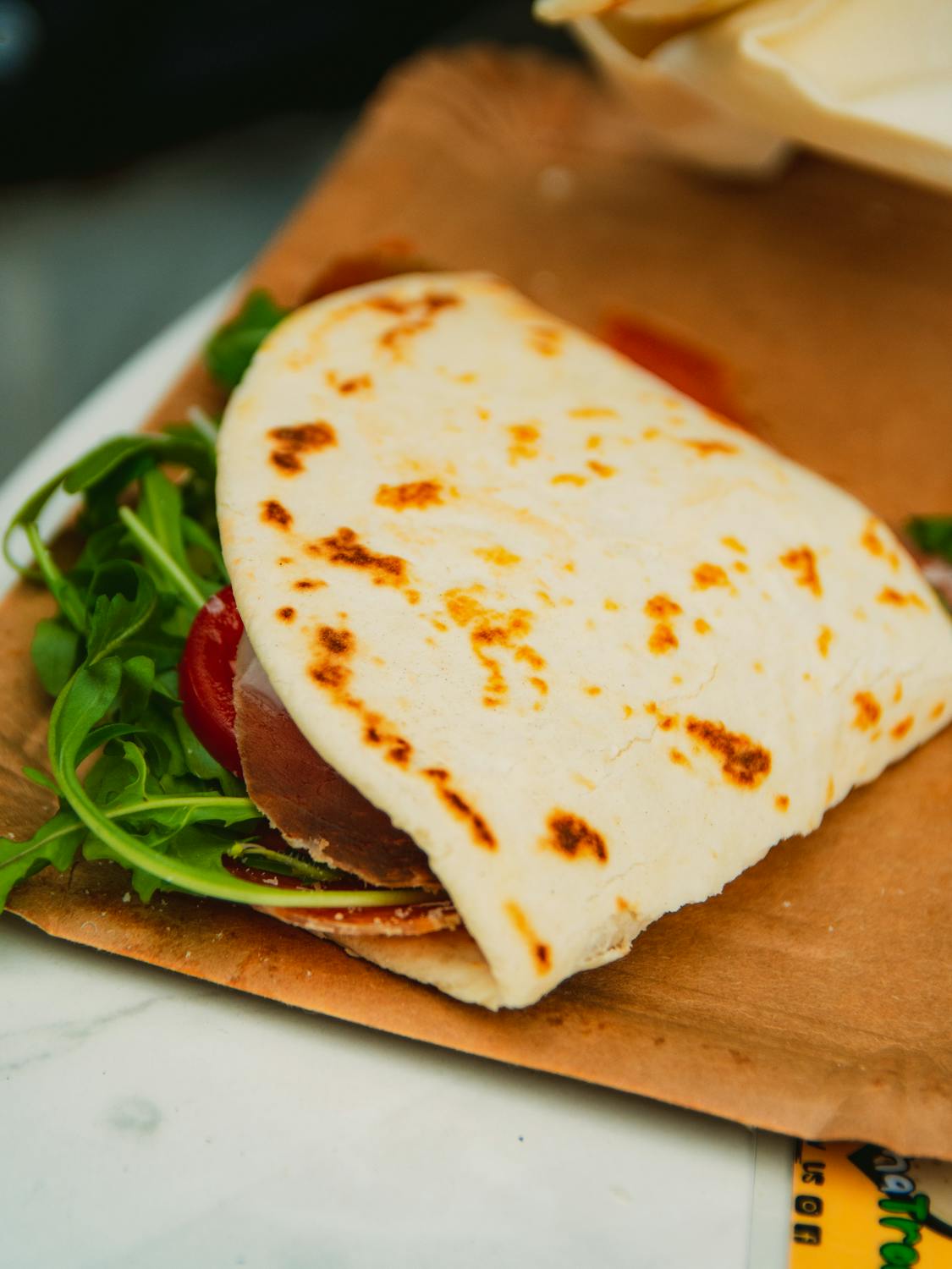 8 Reasons Burger Lovers Are Sleeping on This Southern Sandwich 1 Tempting piadina romagnola filled with arugula, prosciutto, and tomato on a paper plate.