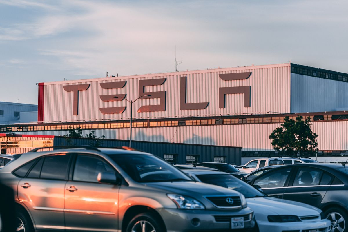 Tesla’s $1.2 Trillion Gamble: Why Elon Musk May Have to Choose Between China and SpaceX 1 Tesla factory with parked cars during sunset, showcasing modern automotive industry vibes.