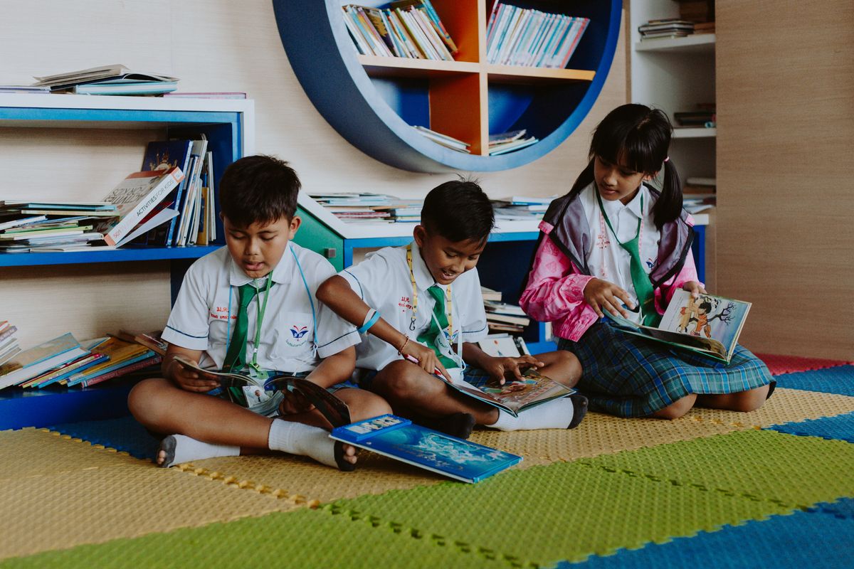 U.S. Education’s 10 Hard Truths: Reading Gaps, $800B Spending, and a System Under Pressure 1 Three children in school uniforms reading books together in a vibrant library setting.