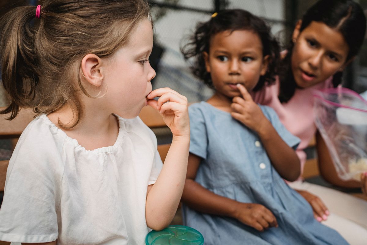 Florida’s Child Hunger Crisis Explodes in 2026: Over 800,000 Kids at Risk 2 Three diverse girls enjoy snacks together, sharing a joyful moment on an outdoor bench.