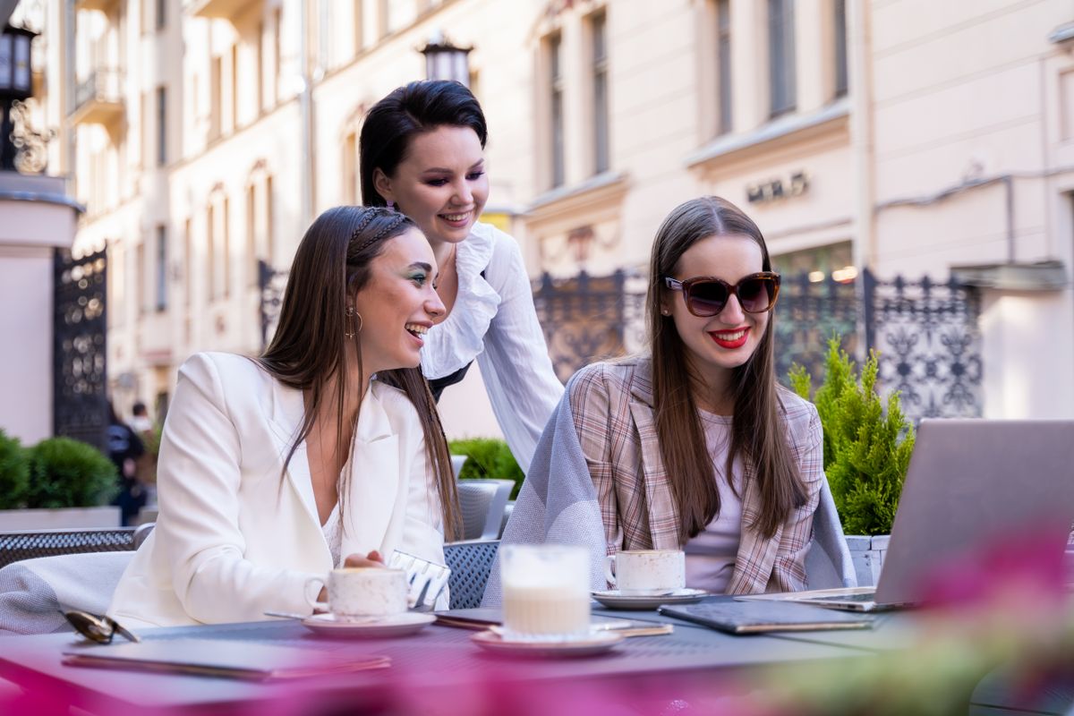 10 Things Retirees Miss About Working That Make Retirement Feel Strangely Empty 2 Three fashionable women enjoy a meeting at an outdoor café with coffee and laptops.