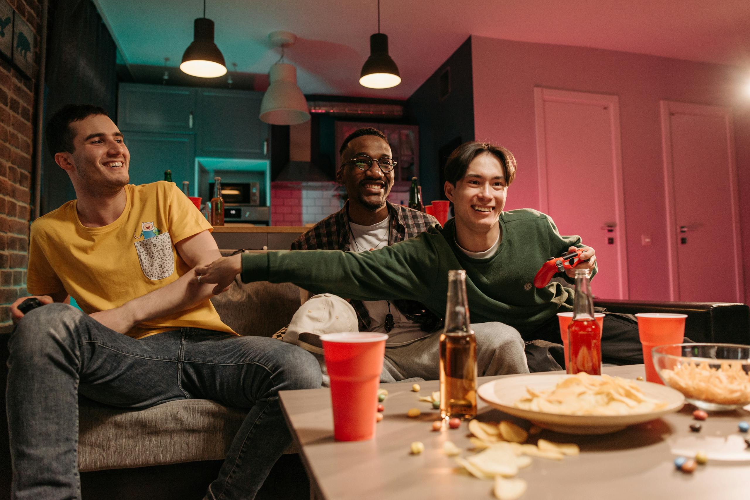 8 quiet marriage pressures that leave men exhausted before they admit it 4 Three friends happily engaging in video games with snacks and drinks in a cozy home setting.
