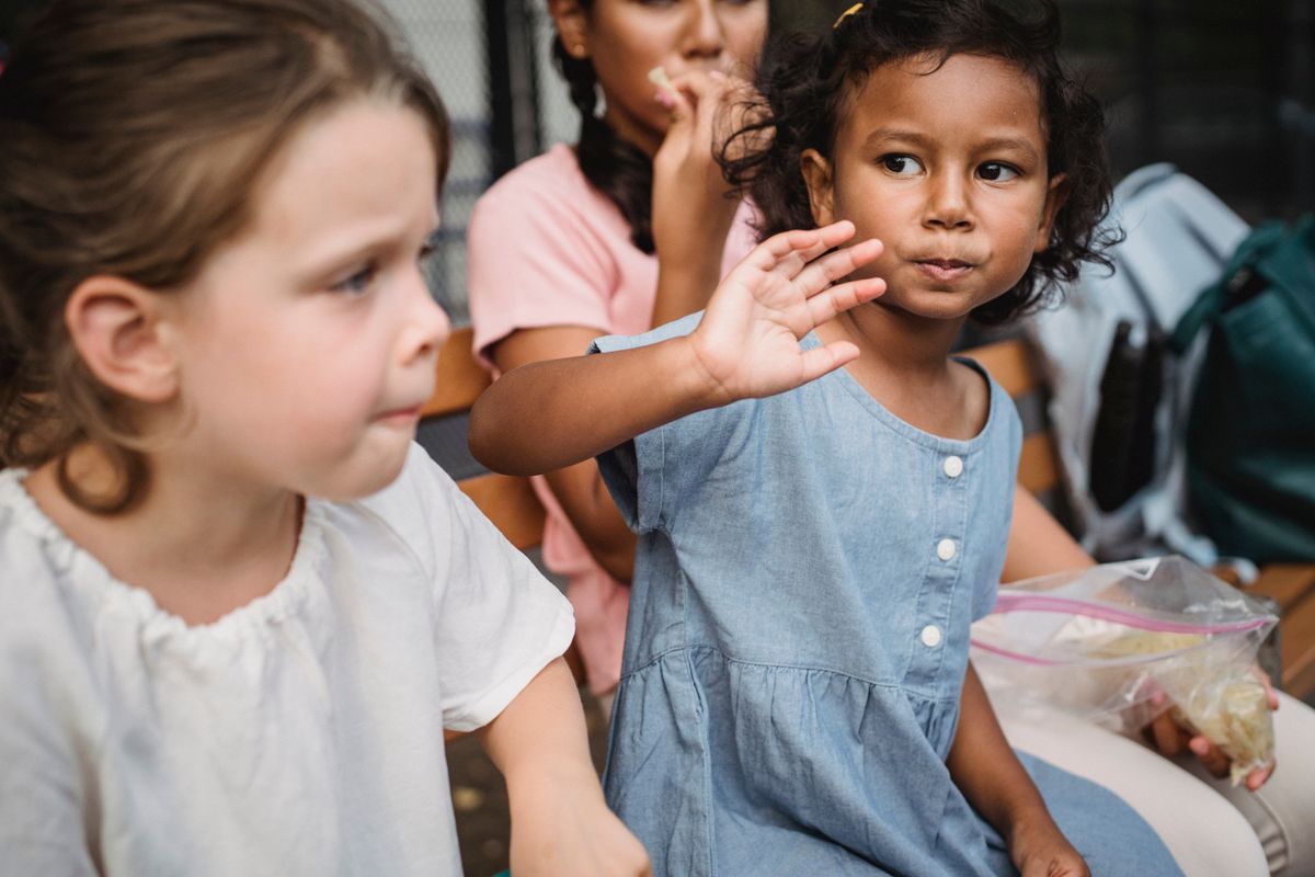 Three young girls sharing a fun snack break together at kindergarten.