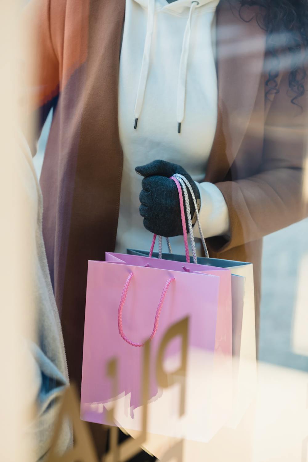 Through glass high angle of crop anonymous female buyer with colorful shopping packets standing near showcase of shop