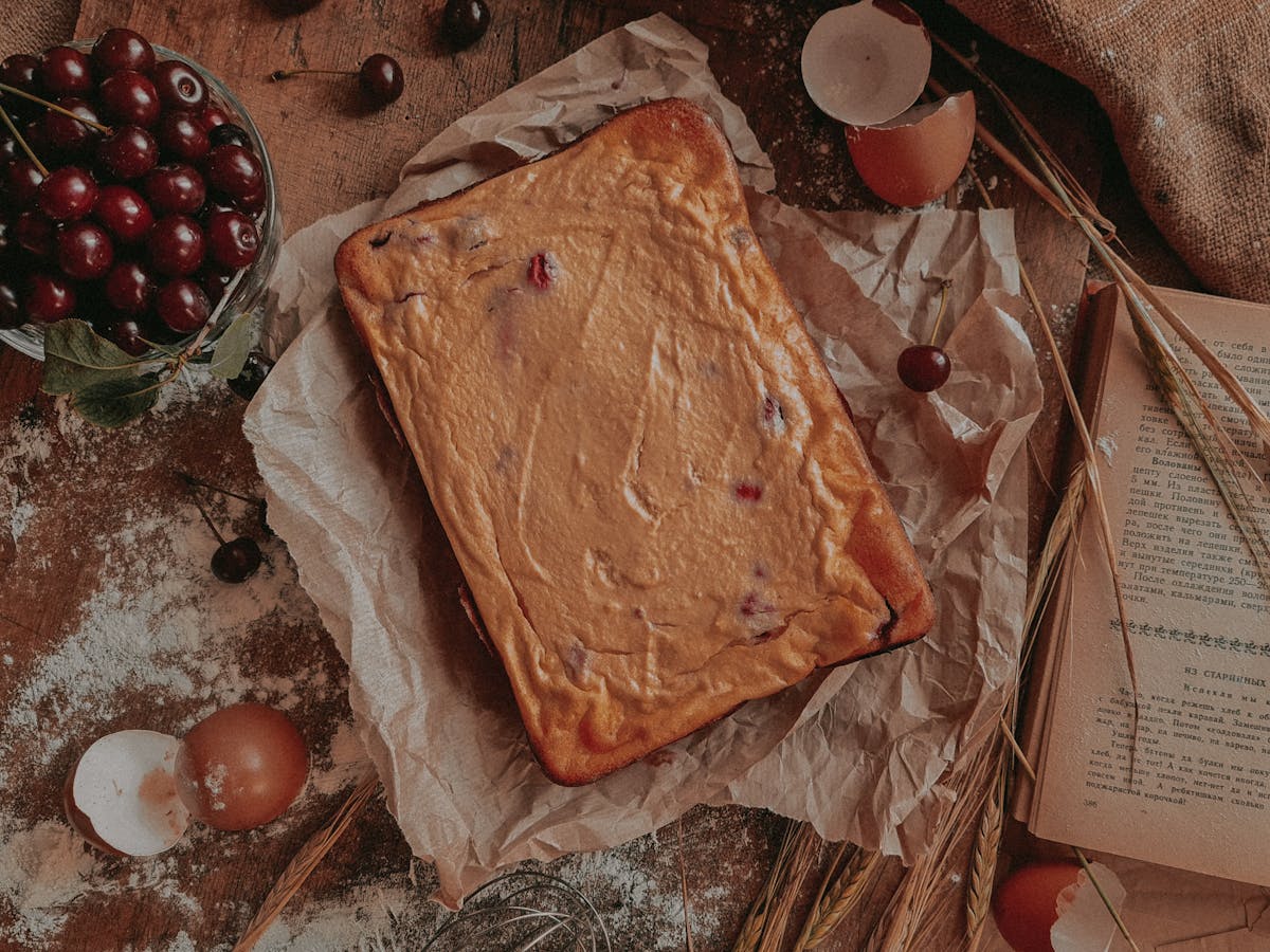 Top view of a homemade cherry cake on brown paper with raw ingredients around for a rustic, cozy feel.