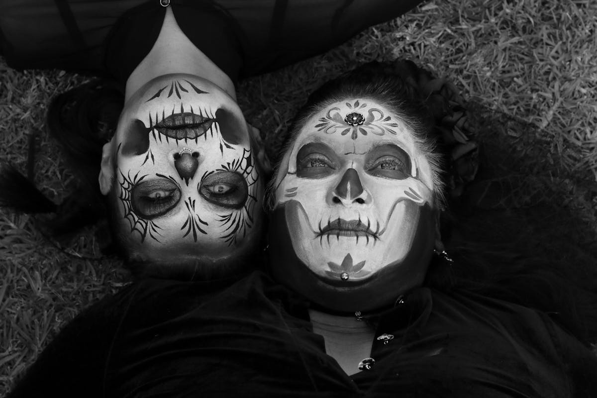 6 Terrifying Realities That Unfold When We Die 2 Two adults with intricate Day of the Dead face paint lie on grass, creating a bold and artistic scene.
