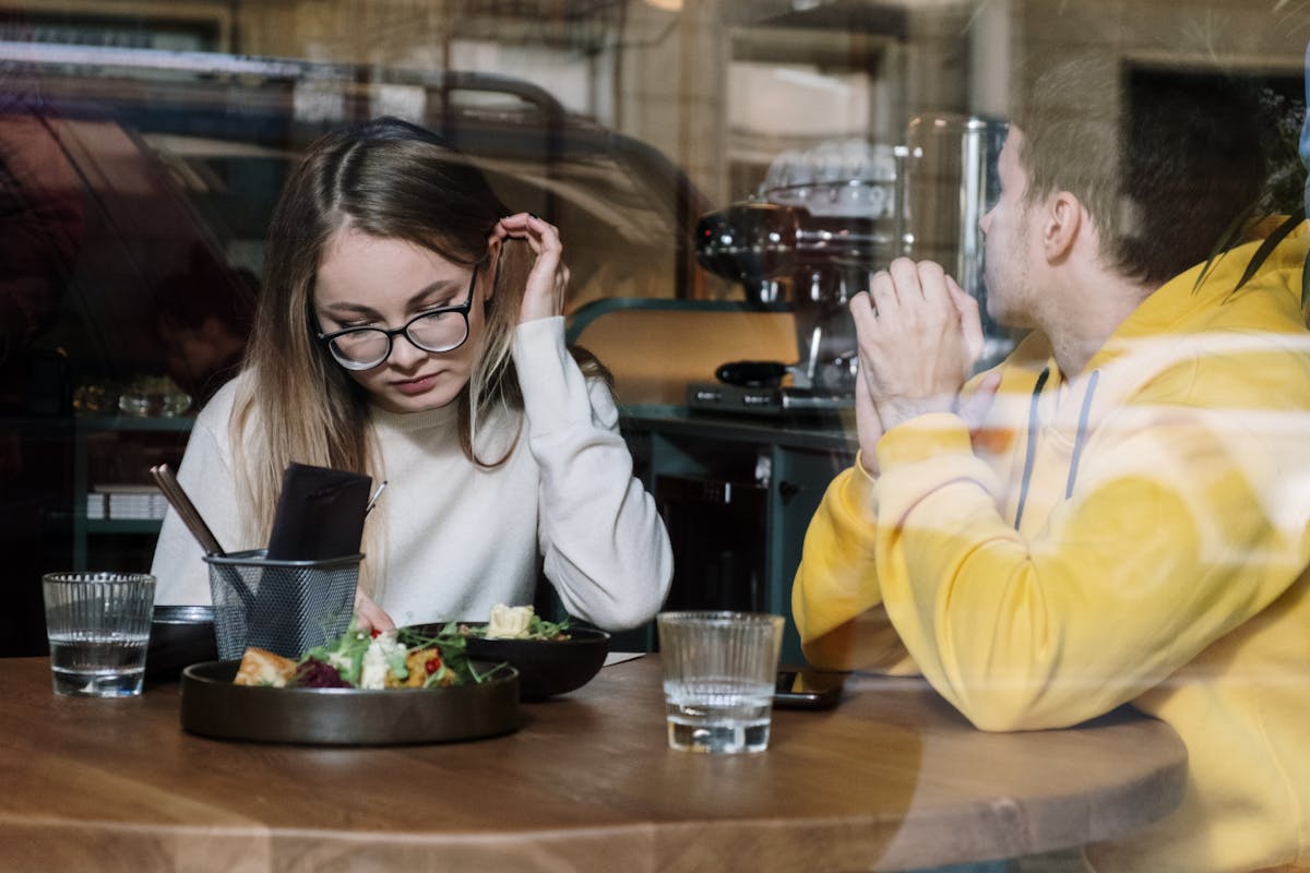 Two friends enjoying a meal at a chic urban cafe, seen through a stylish window.