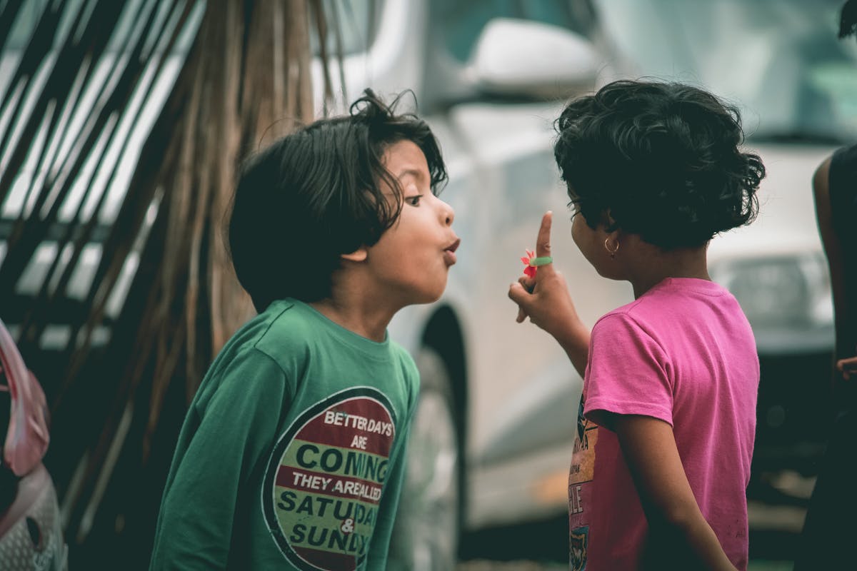 Two kids enjoying an animated conversation outside with playful expressions and gestures.