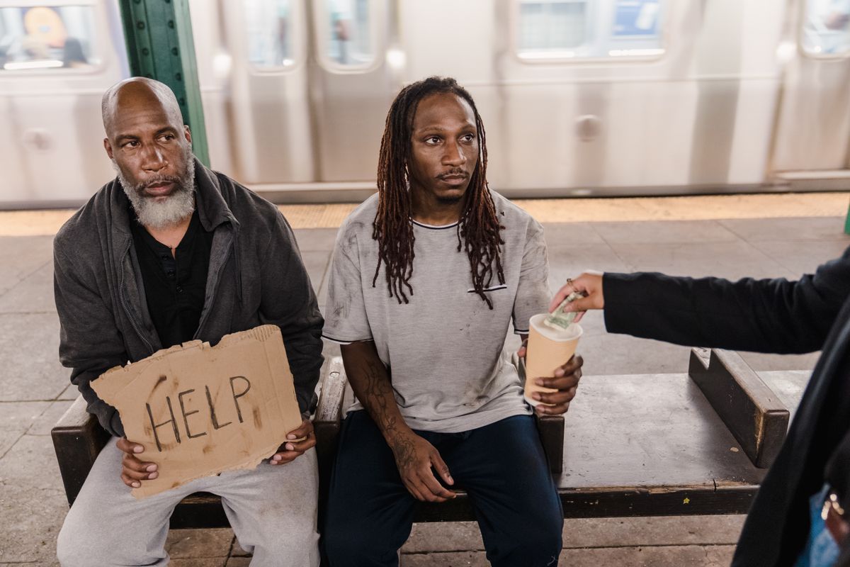 Two men in a subway station seeking help, with a passerby offering money.