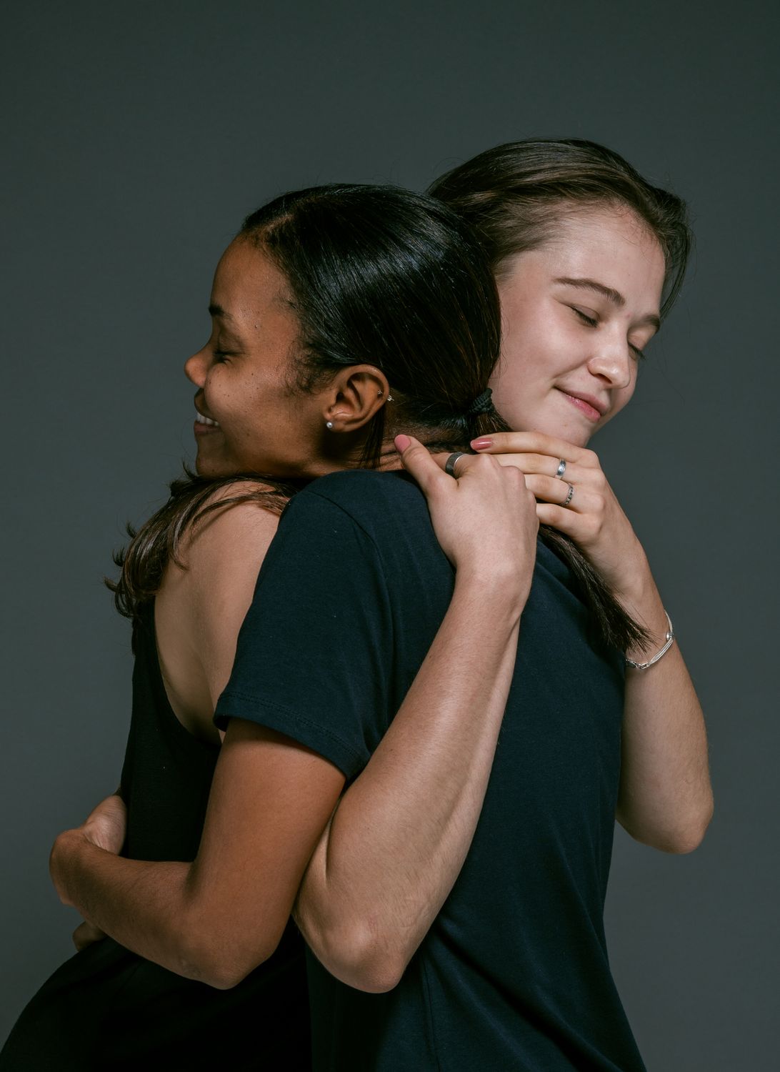 11 Painful Signs God Has Forgiven You, Even If Guilt Still Follows You 2 Two women of different ethnicities share a warm hug, symbolizing love and friendship against a gray backdrop.