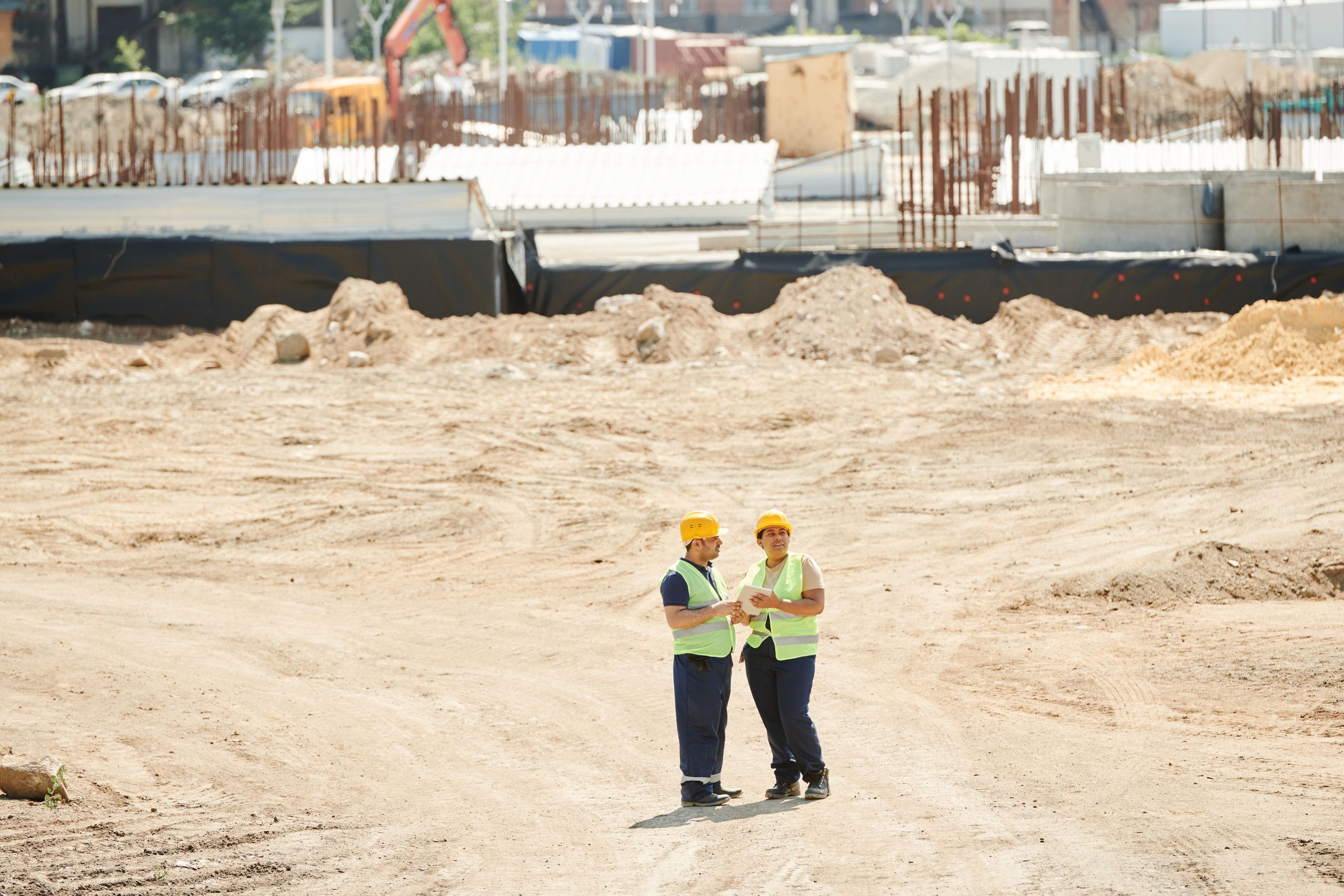 South Florida’s Housing Crisis Is Deepening as the Live Local Act Faces a Brutal Worker Affordability Test 1 Two workers discussing plans on a sandy construction site, wearing safety gear.