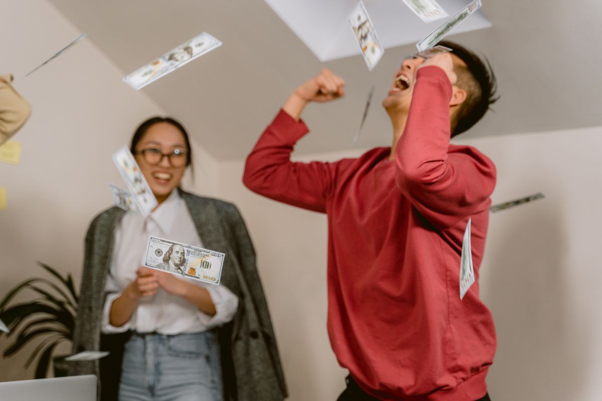 13 Costly Will Mistakes That Can Leave Families Fighting After You’re Gone 4 Two young adults in a room celebrating with falling dollar bills, expressing excitement and joy.