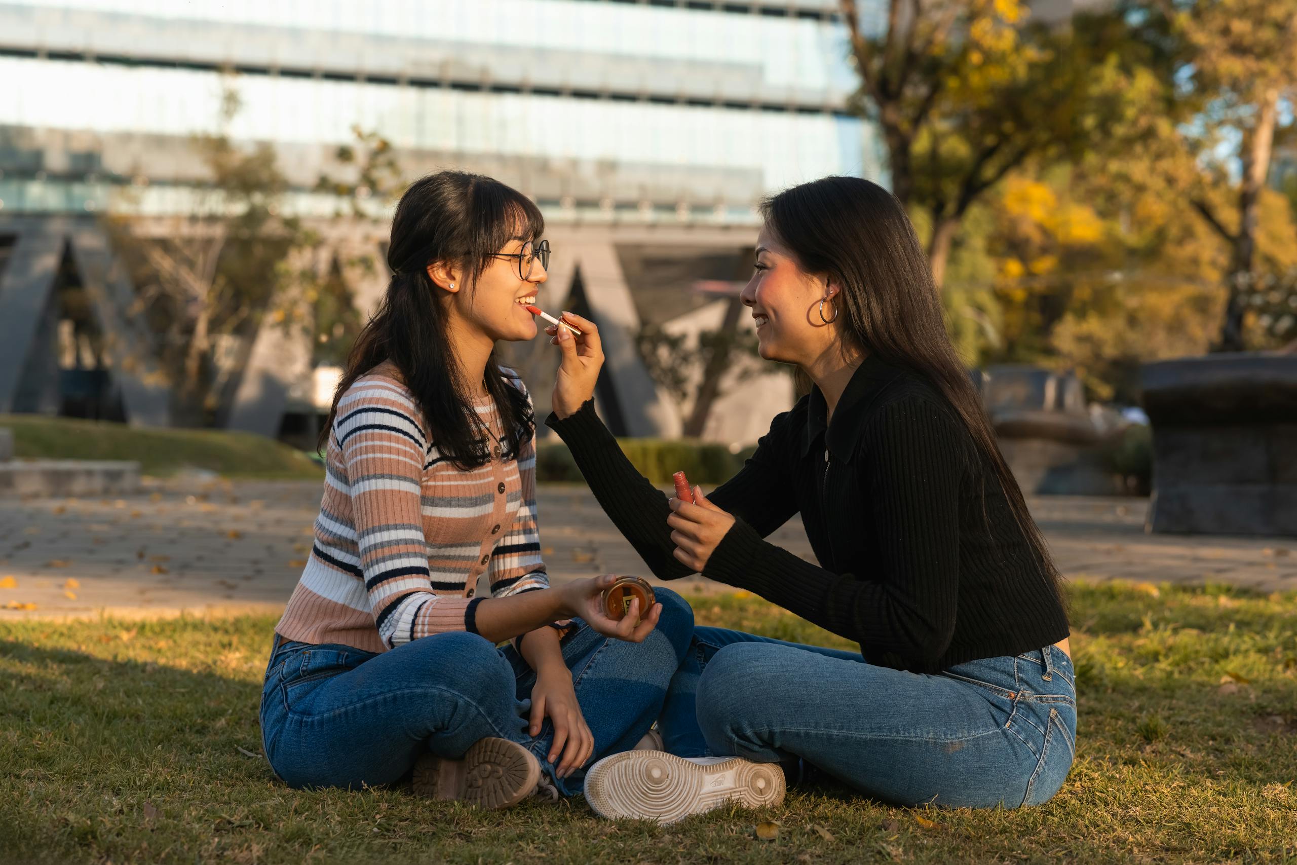 8 Gross Things People Put Near Their Mouth Without Thinking 3 Two young women sitting on grass, sharing snacks in a sunny park setting.