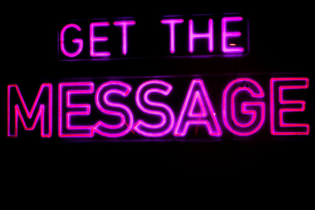 Vibrant pink neon sign with phrase 'Get the Message' against a dark background.