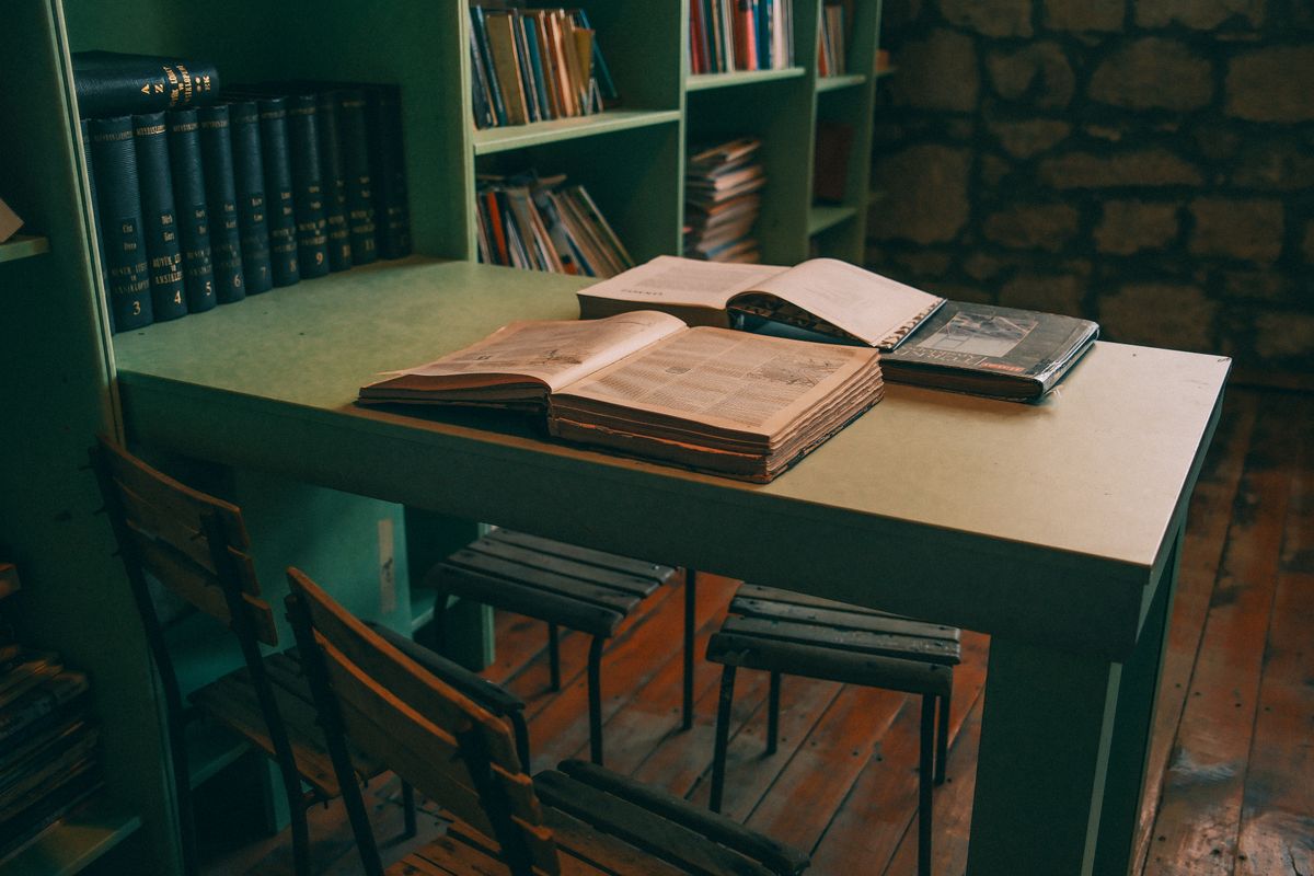 Brutally Relatable Things That Take Over ADHD Homes 1 Warm-toned library interior featuring open books on a vintage table with green shelves.