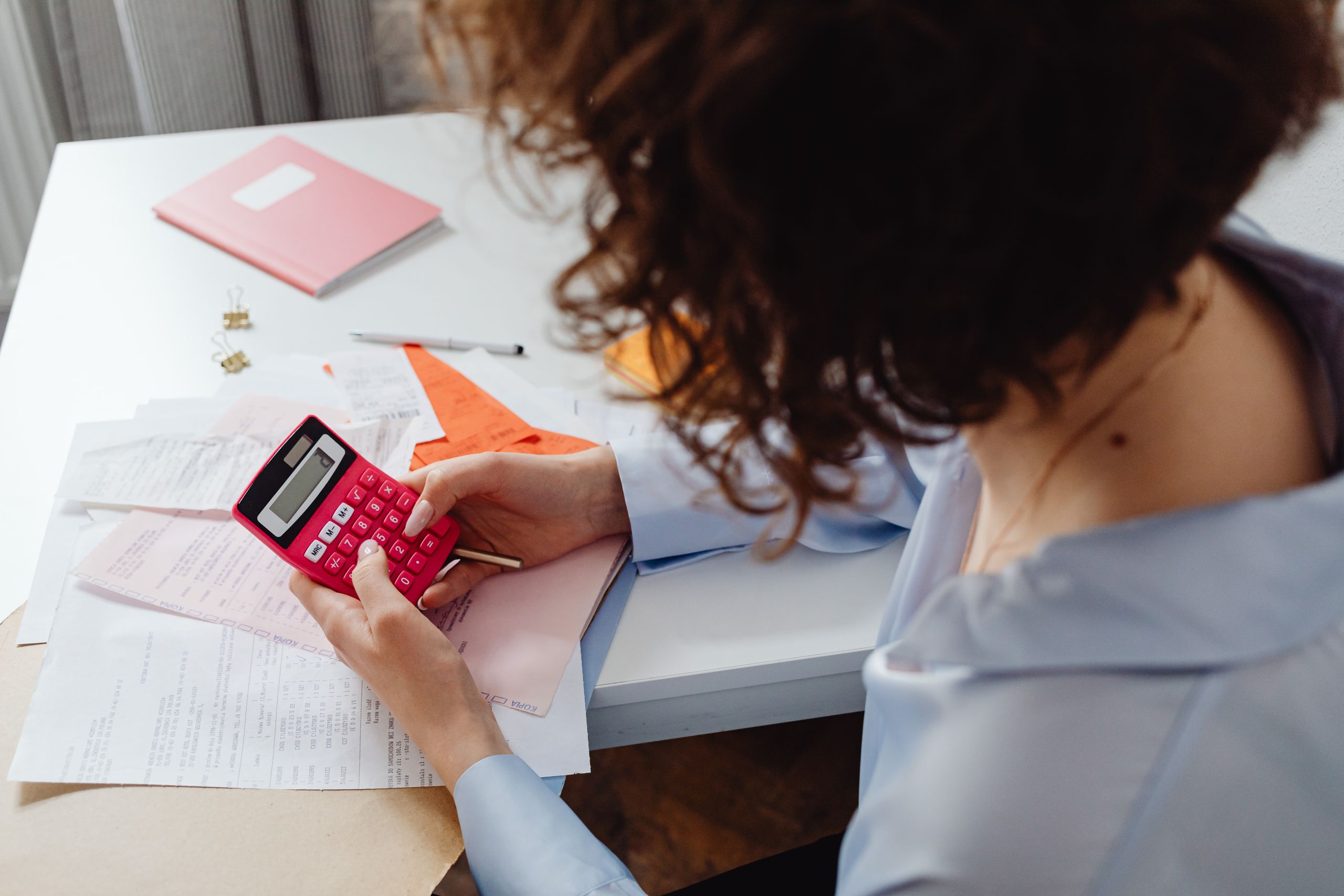 Woman calculating expenses with documents and calculator at work desk.