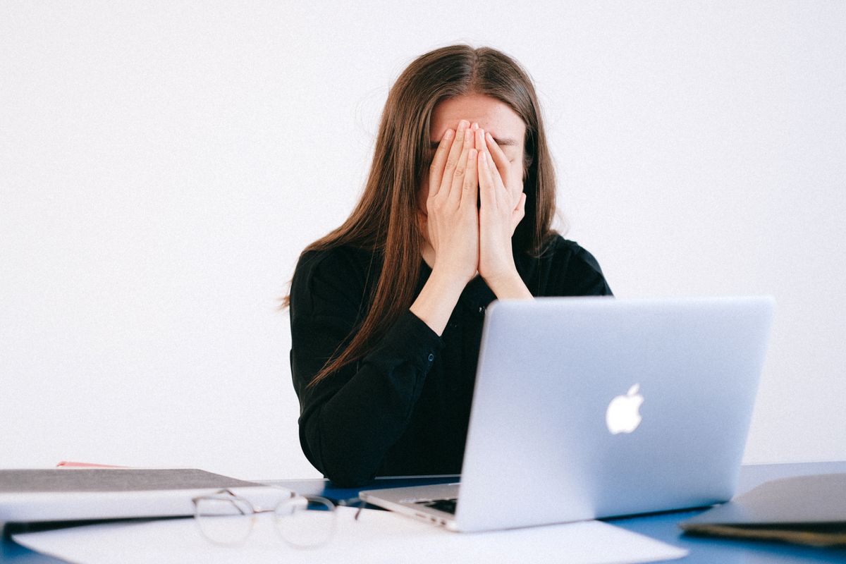Woman feeling stressed and overwhelmed at her desk while working remotely on a laptop. burnout