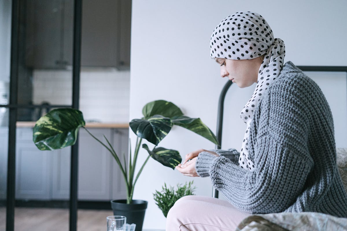Terrifying Cancer Symptoms People Ignore Until It's Too Late 3 Woman in headscarf sitting indoors, taking medication, symbolizing cancer care and support.