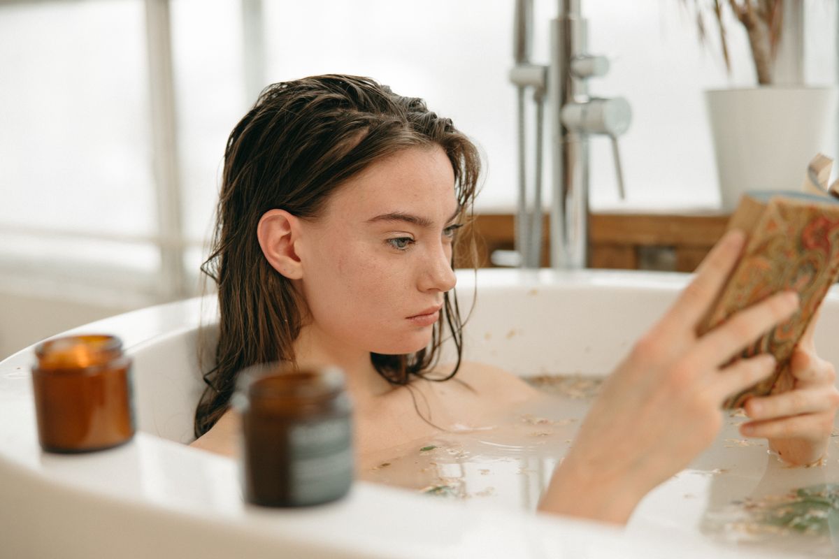 Woman relaxing in a bathtub with a book and candles, enjoying a calming ritual.