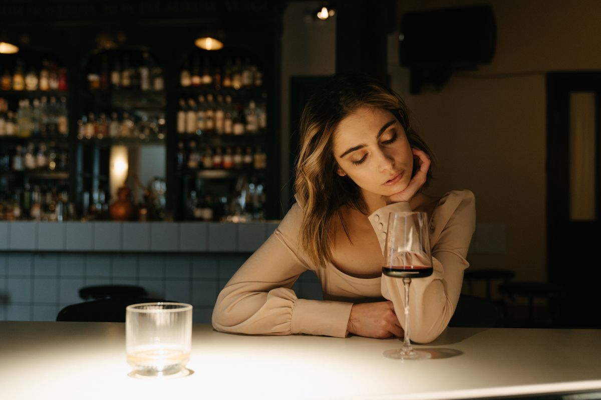 Woman sitting in a bar, elegantly holding a wine glass in a dimly lit, inviting atmosphere.