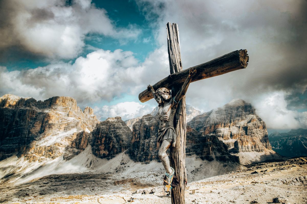 Wooden crucifix against a dramatic mountain backdrop with clouds.